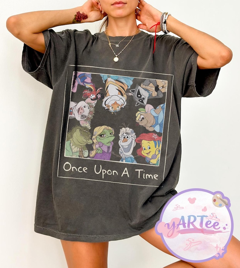 May include: Dark gray t-shirt featuring a rectangular graphic with cartoon characters and the text "Once Upon A Time." The graphic includes a variety of animated figures. The shirt has short sleeves and a relaxed fit.