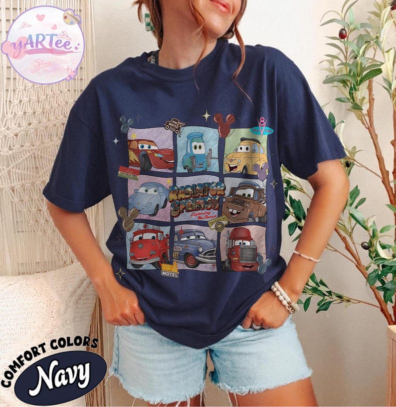 May include: Navy blue t-shirt featuring a grid of cartoon cars from the movie Cars. The shirt has the words "Radiator Springs" and "Lightning McQueen" printed on it. The shirt is made of a soft, comfortable material.