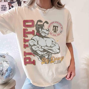 May include: Cream-colored t-shirt featuring a muscular dog graphic with the text "PITTO" in maroon and "Big Dawg Club" in gold. The shirt also includes a "Toontown Athletic Div" logo.