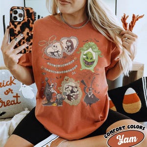 Puede incluir: Camiseta naranja quemado con ilustraciones enmarcadas de personajes de The Nightmare Before Christmas. La camiseta incluye a Jack Skellington, Sally, Oogie Boogie y otros personajes. El texto en la camiseta dice "The Nightmare Before Christmas".
