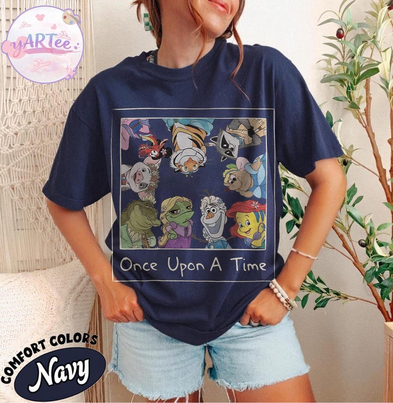 May include: Navy blue t-shirt featuring a colorful graphic of cartoon characters from various animated films. The graphic is framed with a white border and includes the text "Once Upon A Time". The shirt is labeled "Comfort Colors Navy".