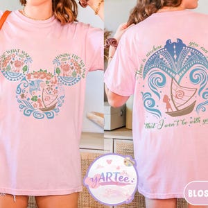 May include: Light pink t-shirt with a Disney-inspired design. The front features a Mickey Mouse head with floral and boat motifs, and the text "COME WHAT MAY" and "KNOW THE WAY". The back has a boat and the text "There is nowhere you can go that I won't be with you..."