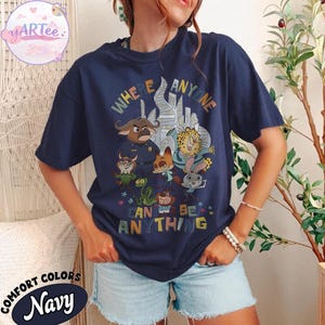 Puede incluir: Camiseta azul marino con un gr&aacute;fico colorido con personajes de dibujos animados y el texto "WHERE ANYONE CAN BE ANYTHING". La camiseta tiene cuello redondo y mangas cortas. La marca "YARtee" es visible en la esquina superior izquierda.