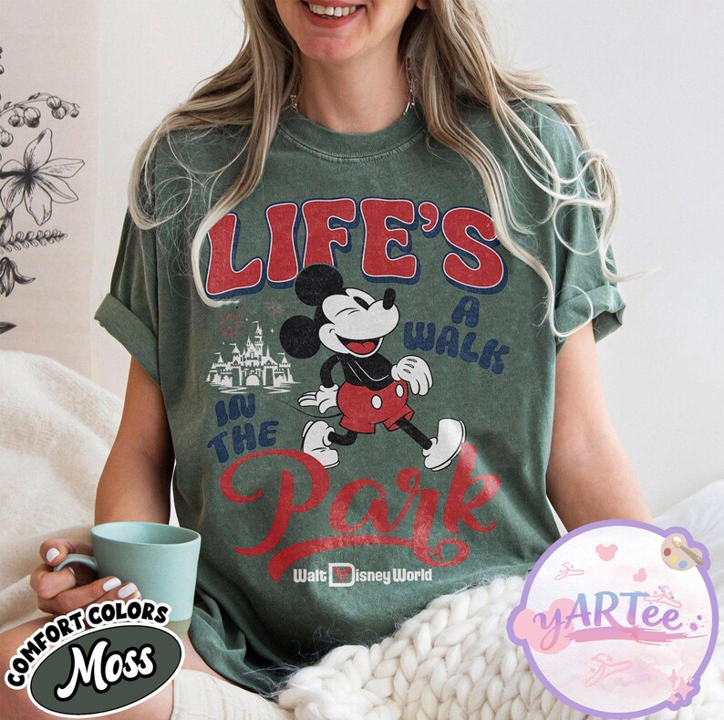 May include: Moss green t-shirt with Mickey Mouse graphic and the text "LIFE'S A WALK IN THE PARK" in red and blue. The shirt also includes the words "Walt Disney World". The shirt is a comfort colors brand.