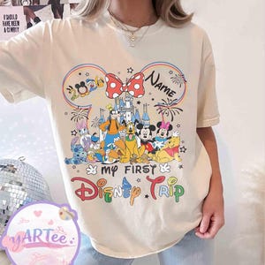 May include: Cream-colored t-shirt featuring a colorful graphic of Disney characters, including Mickey and Minnie Mouse, Goofy, and Winnie the Pooh. The design includes the text "My First Disney Trip" and "2024". A red bow with white polka dots is also featured.