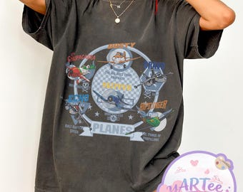 Puede incluir: Camiseta gris oscuro con un diseño de aviones de dibujos animados y el texto "Planes". El diseño incluye nombres de personajes como "Dusty" y "Chupacabra". El diseño está centrado en la parte delantera.