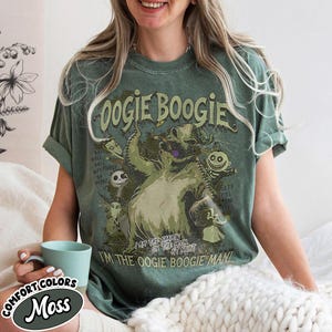 Puede incluir: Una camiseta verde musgo con el texto "Oogie Boogie" y un gr&aacute;fico del personaje de Pesadilla antes de Navidad. La camiseta tambi&eacute;n incluye el texto "I'm the Oogie Boogie Man!" y "Comfort Colors Moss".