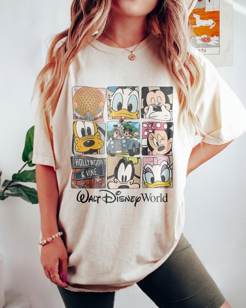 Op de afbeelding: Een beige T-shirt met een grafische print van verschillende Disney-figuren, waaronder Mickey Mouse, Minnie Mouse, Donald Duck, Goofy en Pluto. De afbeelding bevat ook een foto van de Spaceship Earth-attractie in Epcot en een bord met de tekst "Hollywood & Vine". De tekst "Walt Disney World" staat onder de afbeelding.