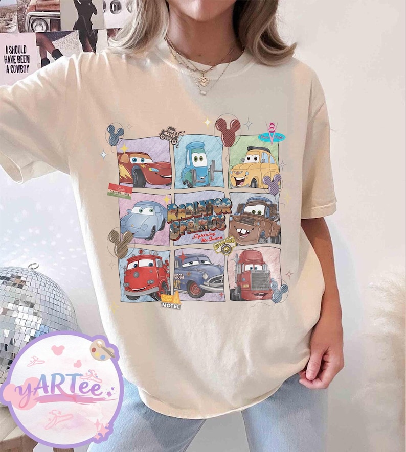 May include: Cream-colored t-shirt featuring a grid of cartoon cars from the movie Cars. The grid includes Lightning McQueen and Mater, with the text "Radiator Springs" and "Lightning McQueen".