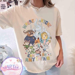 Puede incluir: Camiseta color crema con un gr&aacute;fico colorido de personajes de dibujos animados y el texto "WHERE ANYONE CAN BE ANYTHING". El dise&ntilde;o presenta personajes de animales en un entorno urbano, con un estilo l&uacute;dico y caprichoso.