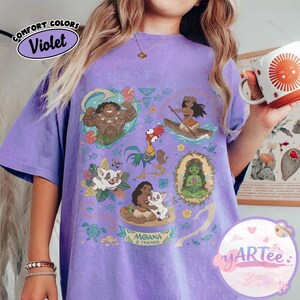 K&ouml;nnte beinhalten: Violettes T-Shirt mit einem Grafikdesign mit Charakteren aus dem Film Moana. Das Design umfasst Illustrationen von Maui, Moana, Hei Hei, Pua und anderen Charakteren. Das Shirt tr&auml;gt auch den Text "MOANA & FRIENDS".