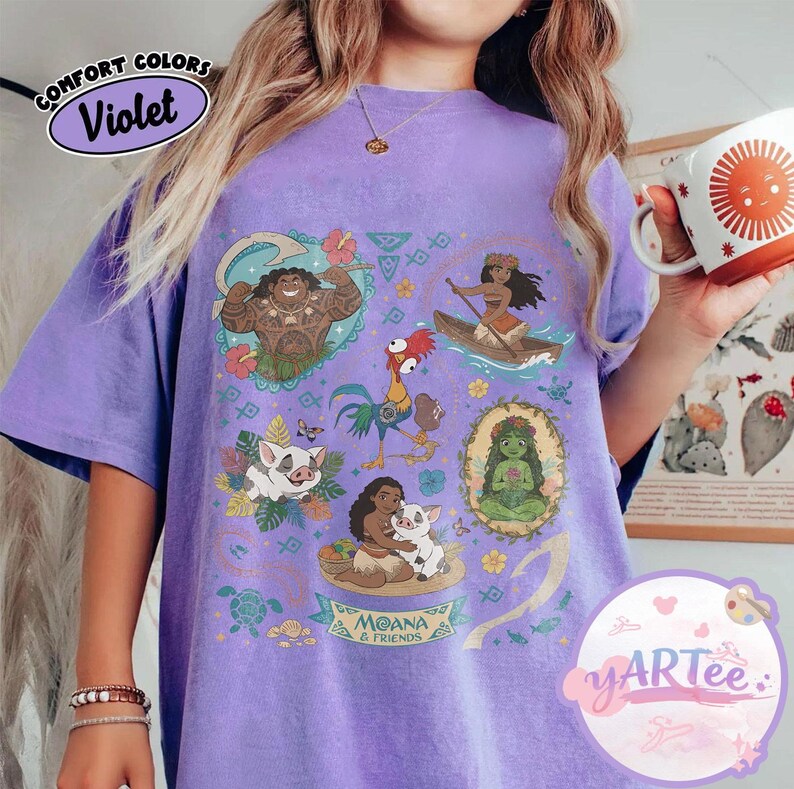 K&ouml;nnte beinhalten: Violettes T-Shirt mit einem Grafikdesign mit Charakteren aus dem Film Moana. Das Design umfasst Illustrationen von Maui, Moana, Hei Hei, Pua und anderen Charakteren. Das Shirt tr&auml;gt auch den Text "MOANA & FRIENDS".