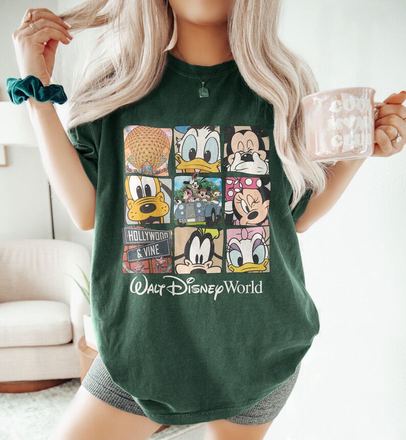 May include: A green t-shirt with a graphic print of various Disney characters, including Mickey Mouse, Donald Duck, Goofy, and Pluto. The graphic is arranged in a grid pattern with each character in a separate square. The t-shirt also has the text 'Hollywood & Vine' and 'Walt Disney World' printed on it.