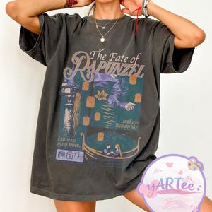 May include: Dark gray t-shirt featuring a graphic from the movie "Tangled". The design includes the text "The Fate of Rapunzel" and a scene with lanterns, a boat, and the text "...until you lit up my sky".