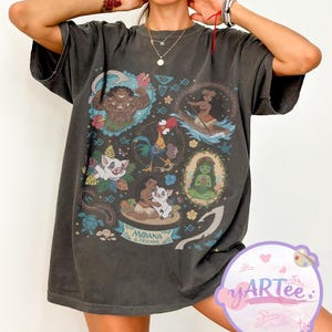 K&ouml;nnte beinhalten: Dunkelgraues T-Shirt mit einer farbenfrohen Grafik von Charakteren aus dem Animationsfilm "Vaiana". Das Design enth&auml;lt Bilder von Maui, Vaiana, Pua, Hei Hei und anderen Charakteren. Die Worte "Moana & Friends" sind ebenfalls sichtbar.