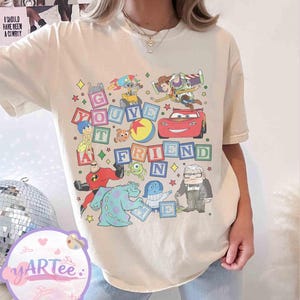 Puede incluir: Camiseta color crema con un gr&aacute;fico colorido de varios personajes animados y la frase "You've Got A Friend". El dise&ntilde;o incluye personajes de pel&iacute;culas de animaci&oacute;n populares, con un tema l&uacute;dico y nost&aacute;lgico.
