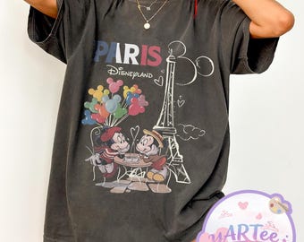 Könnte beinhalten: Dunkelgraues T-Shirt mit einem Motiv von Mickey und Minnie Mouse in Paris, Frankreich. Das Design zeigt den Eiffelturm, Ballons und den Text "PARIS Disneyland". Das T-Shirt hat kurze Ärmel und eine lockere Passform.
