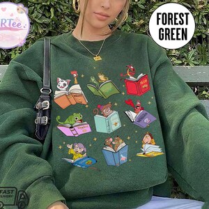 Puede incluir: Sudadera verde bosque con ilustraciones coloridas de personajes animados leyendo libros. La sudadera tiene cuello redondo y mangas largas. El texto "Forest Green" est&aacute; impreso en la parte superior derecha.