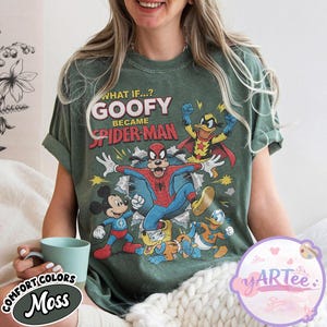 May include: A moss green t-shirt with a graphic of Goofy as Spider-Man and other Disney characters. The text reads "WHAT IF...? GOOFY BECAME SPIDER-MAN". The shirt has a vintage, distressed appearance.