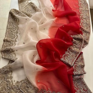 May include: A white and red ombre chiffon saree with gold embroidery. The saree has a delicate, flowing fabric and intricate details.