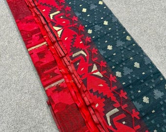 May include: A folded textile with a dark teal background and a red border. The border features a repeating geometric design in red and white. Small gold-colored floral accents are scattered across the teal fabric.
