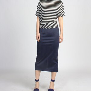 Może przedstawiać: Kobieta w czarno-białej paskowanej bluzie, granatowej spódnicy i ciemnoniebieskich sandałach na obcasie.