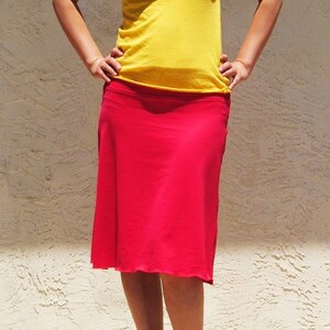 May include: A bright yellow sleeveless tank top with a scoop neckline paired with a solid red knee-length skirt. The skirt features a smooth, straight-cut silhouette that falls just below the knees, complemented by black open-toe high heel shoes.
