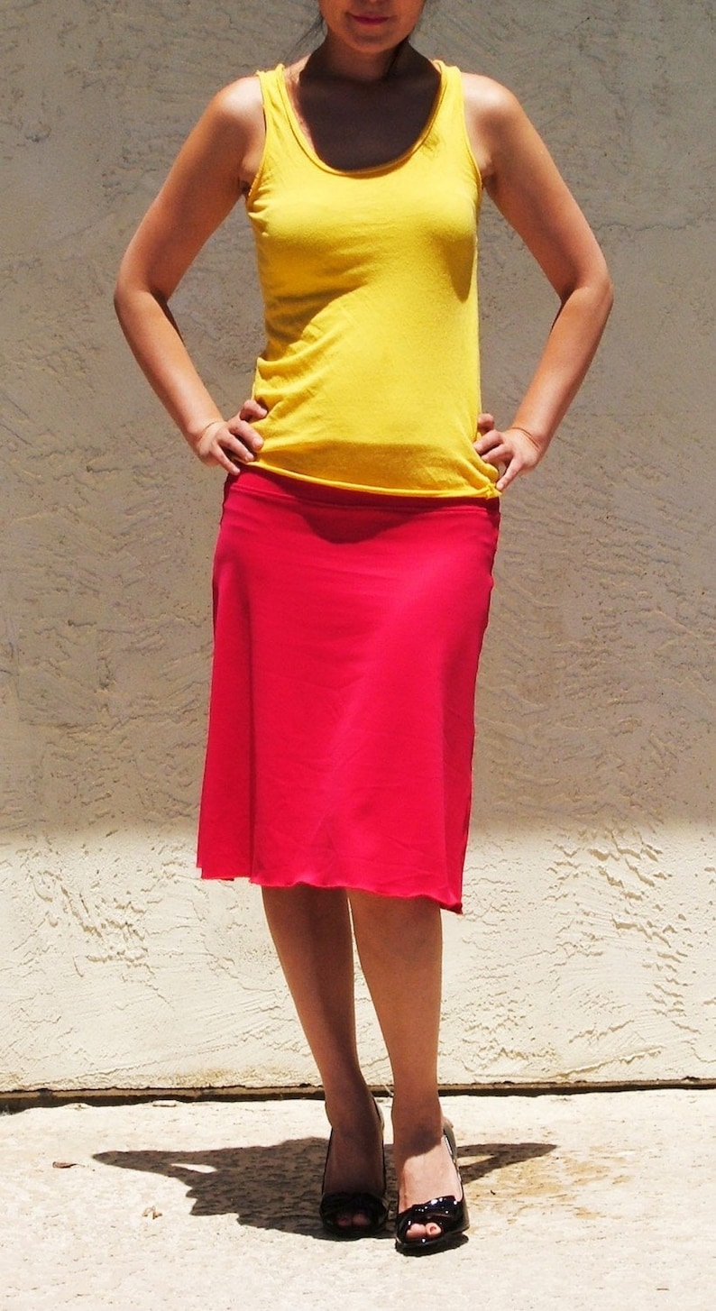 May include: A bright yellow sleeveless tank top with a scoop neckline paired with a solid red knee-length skirt. The skirt features a smooth, straight-cut silhouette that falls just below the knees, complemented by black open-toe high heel shoes.