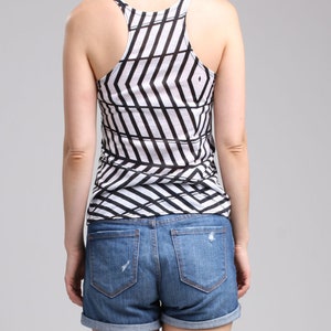 May include: A racerback tank top featuring a white and black geometric chevron pattern paired with blue denim shorts that have a cuffed hem and distressed detailing on the back pockets. The tank top has a scoop neckline and a sleeveless design.