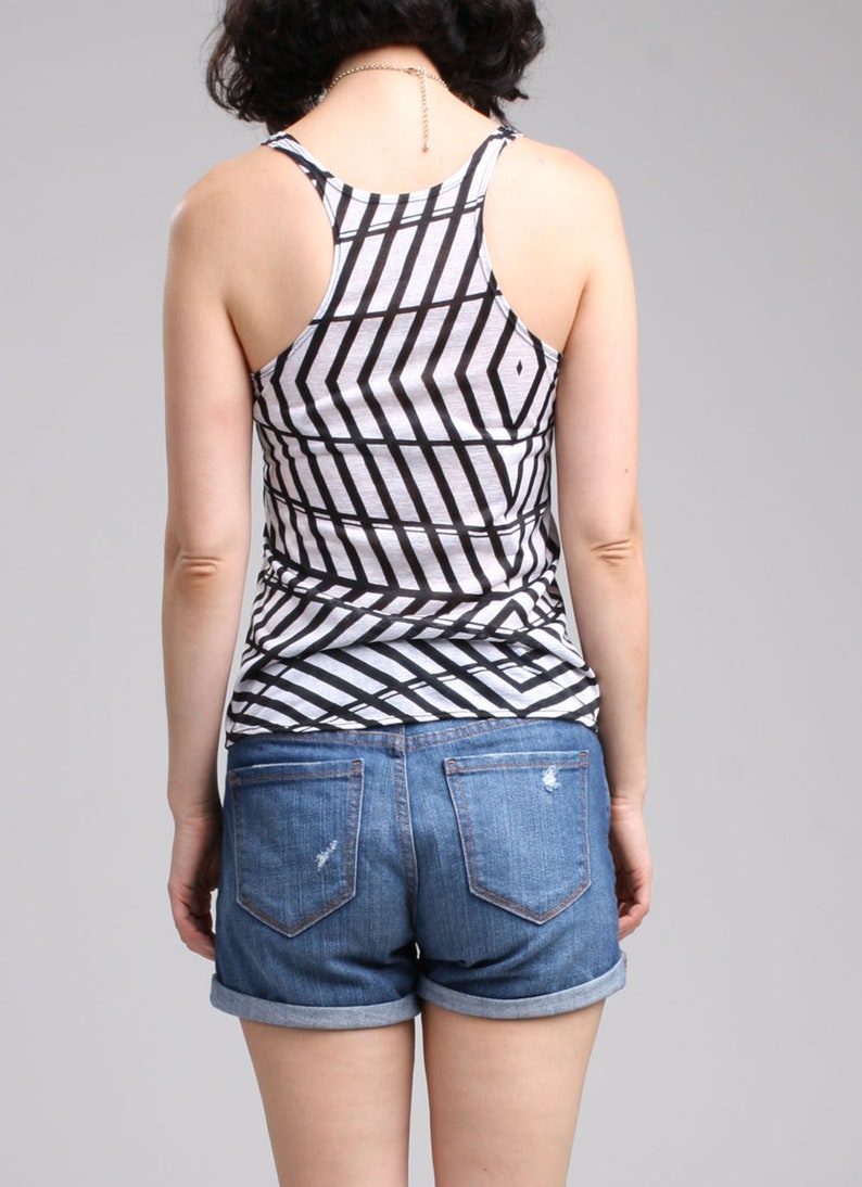 May include: A racerback tank top featuring a white and black geometric chevron pattern paired with blue denim shorts that have a cuffed hem and distressed detailing on the back pockets. The tank top has a scoop neckline and a sleeveless design.