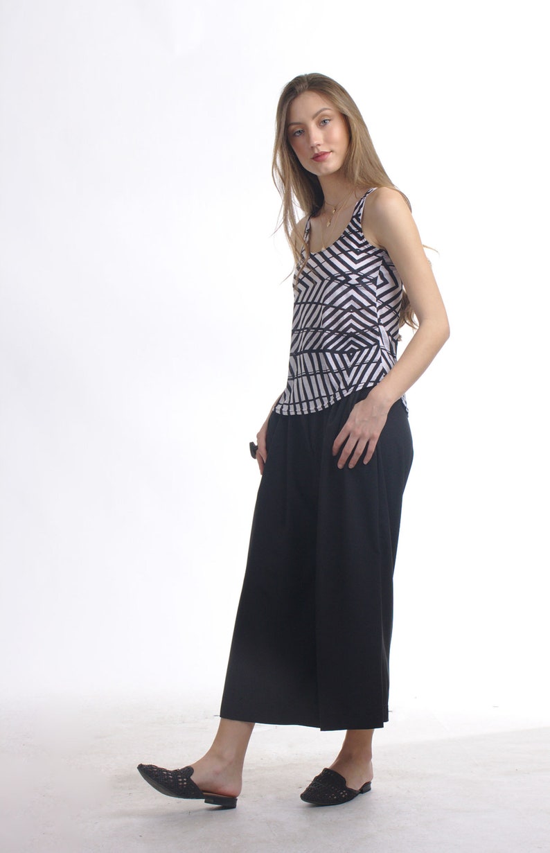May include: A sleeveless tank top featuring a black and white geometric chevron pattern paired with solid black wide-leg cropped trousers and black woven slip-on shoes. The top has a scoop neckline and the trousers have a loose, flowing fit.