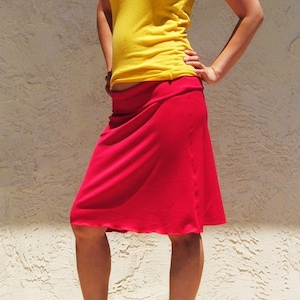 May include: A bright yellow sleeveless tank top with a scoop neckline paired with a knee-length red skirt featuring a wide, folded waistband. The outfit is completed with black high-heeled peep-toe shoes that have a small bow detail on the front.