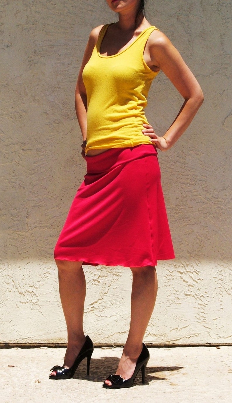 May include: A bright yellow sleeveless tank top with a scoop neckline paired with a knee-length red skirt featuring a wide, folded waistband. The outfit is completed with black high-heeled peep-toe shoes that have a small bow detail on the front.