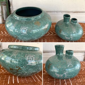 May include: Two green ceramic vases with white geometric designs. The larger vase is wider and rounder, while the smaller vase has two openings at the top.