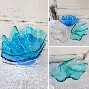May include: Three glass bowls in a seashell shape. The bowls are layered on top of each other. The top bowl is blue and clear, the middle bowl is blue and clear, and the bottom bowl is clear.
