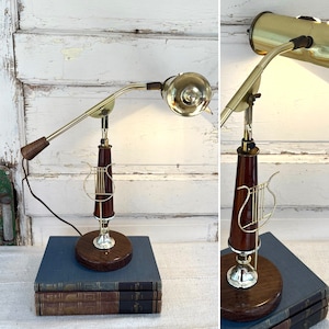 May include: A gold and brown desk lamp with a harp-shaped base. The lamp has a flexible arm and a round, gold shade. The lamp is sitting on a stack of books.
