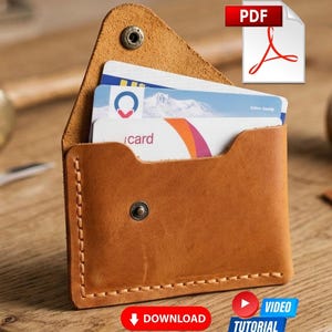 May include: A tan leather card holder with visible stitching along the edges, featuring a triangular flap secured by a metal snap button. The wallet contains three stacked plastic cards with visible text and graphics, including a mountain landscape image.
