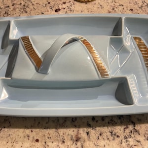 May include: A light blue ceramic serving tray with gold accents. The tray has four sections, including a lid with a handle.