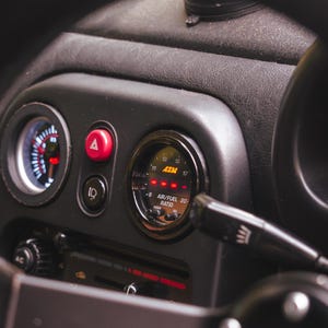 Peut inclure: Un int&eacute;rieur de tableau de bord de voiture avec un volant noir dot&eacute; d'un rep&egrave;re sup&eacute;rieur jaune, une jauge de rapport air/carburant AEM circulaire avec affichage num&eacute;rique rouge, un bouton de feux de d&eacute;tresse rouge et un lecteur DVD.