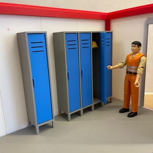Puede incluir: Una escena en miniatura con taquillas azules y grises con un borde rojo. Una taquilla está abierta, revelando un casco amarillo. Una figura con ropa de trabajo naranja está cerca. La escena está ambientada en una habitación con suelo gris.