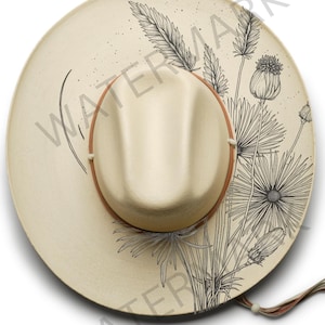 May include: Cream-colored hat with a brown band and a floral design. The hat features a wide brim and a beige crown. The floral design is in black ink and includes various flowers and leaves. The hat has a string attached to the brim.