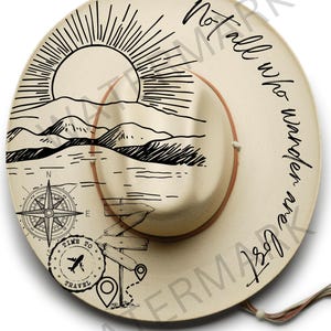 May include: A beige straw hat with a black and white design featuring a sun, mountains, a compass, a plane, and the text "Not all who wander are lost".