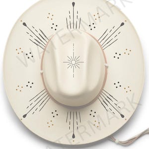 May include: A white cowboy hat with a black and gold geometric design. The design features a sunburst with radiating lines and dots.