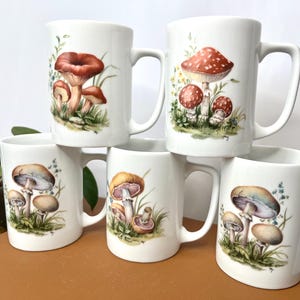 Pu&ograve; includere: Tazze in ceramica bianca con illustrazioni di funghi. Le tazze presentano diversi disegni di funghi nei toni del rosso, marrone e beige, con accenti di erba e fogliame verdi. Ogni tazza ha un manico curvo. Adatte per caff&egrave; o t&egrave;.