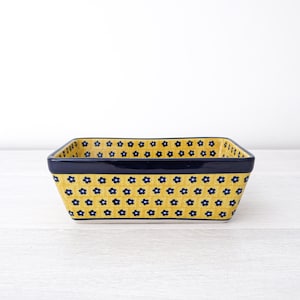 May include: A yellow ceramic baking dish with a blue floral pattern. The dish has a rectangular shape and a slightly raised rim.