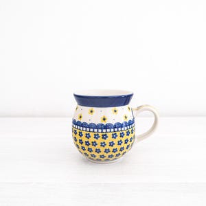 May include: A blue and yellow ceramic mug with a floral pattern. The mug has a rounded body and a handle.