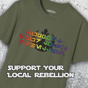 Peut inclure: Un t-shirt vert avec un symbole de l'Alliance rebelle arc-en-ciel et le texte "SUPPORT YOUR LOCAL REBELLION".