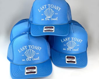 May include: Three blue trucker hats with a white logo that says "Last Toast est 2025 on the coast" and a white seashell graphic. The hats have a mesh back.
