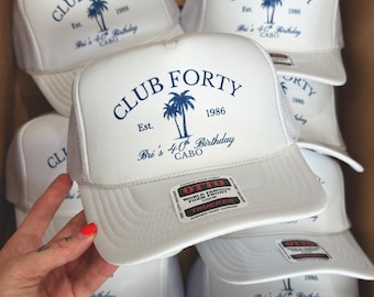 May include: A white trucker hat featuring a blue graphic with a palm tree and the text CLUB FORTY Est. 1986 Bri's 40th Birthday CABO. The hat has a foam front, mesh back, and a sticker on the brim that reads OTTO WORLD FAMOUS FOAM FRONT TRUCKER.