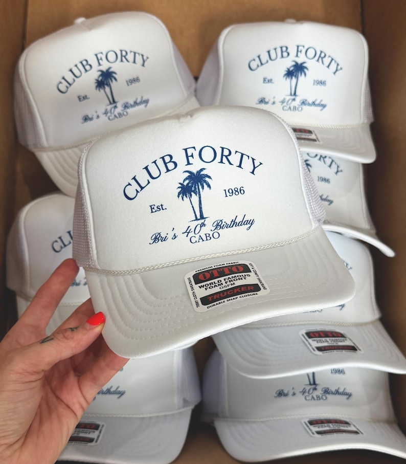 May include: White trucker hats with the text "CLUB FORTY" and "Bri's 40th Birthday CABO" printed in navy blue. The hats feature a palm tree graphic and the year 1986. The hats have a mesh back and a snap closure.